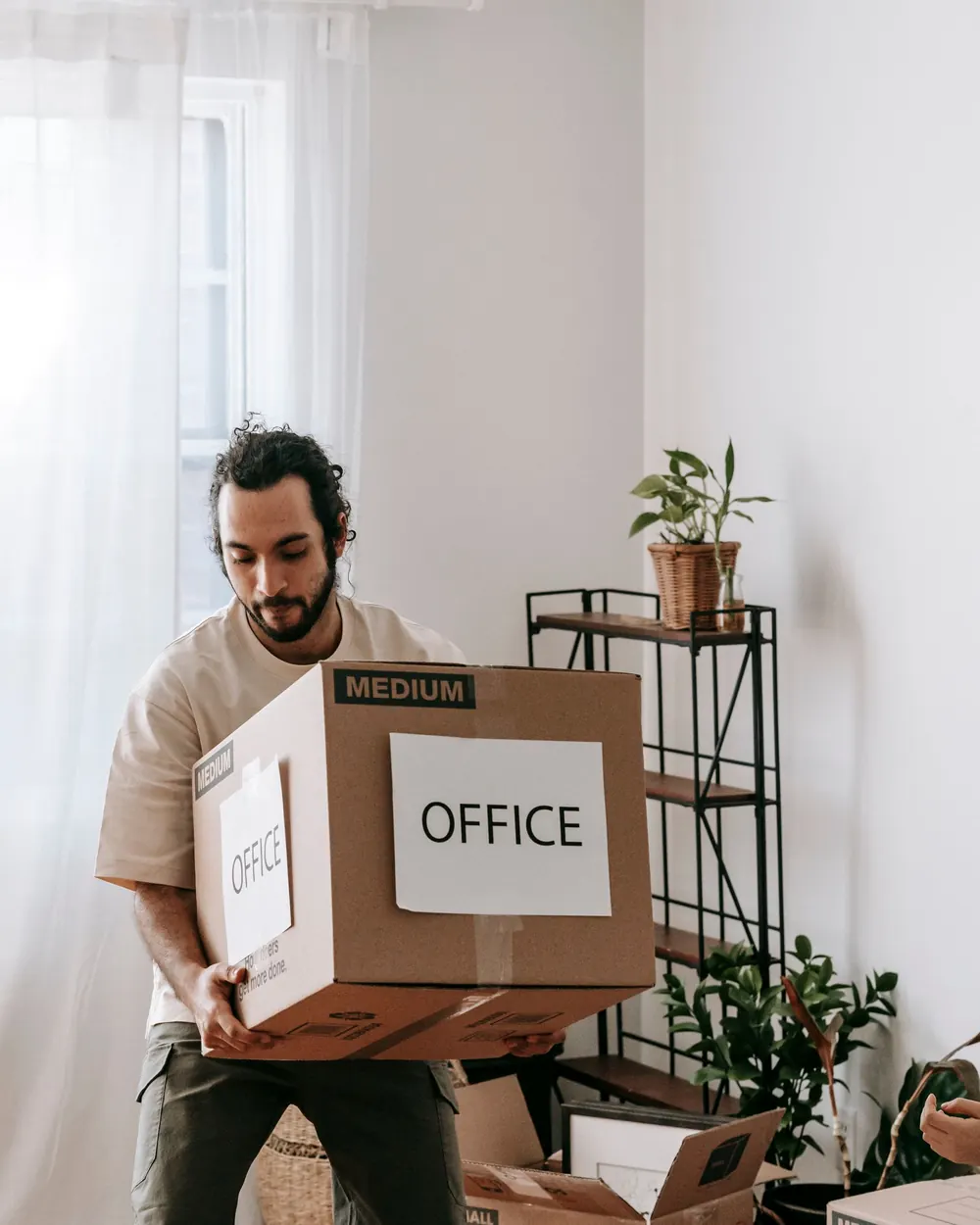 A mover carrying a carton labelled office through a bright room